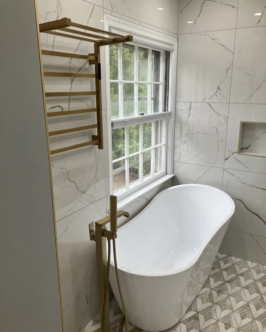 Freestanding tub under a window with a gold towel warmer