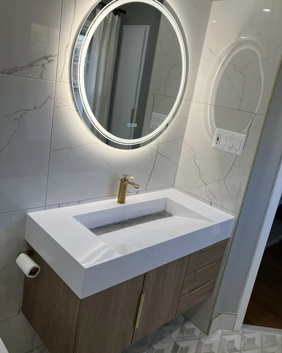 Floating vanity with a trough sink and a round backlit mirror